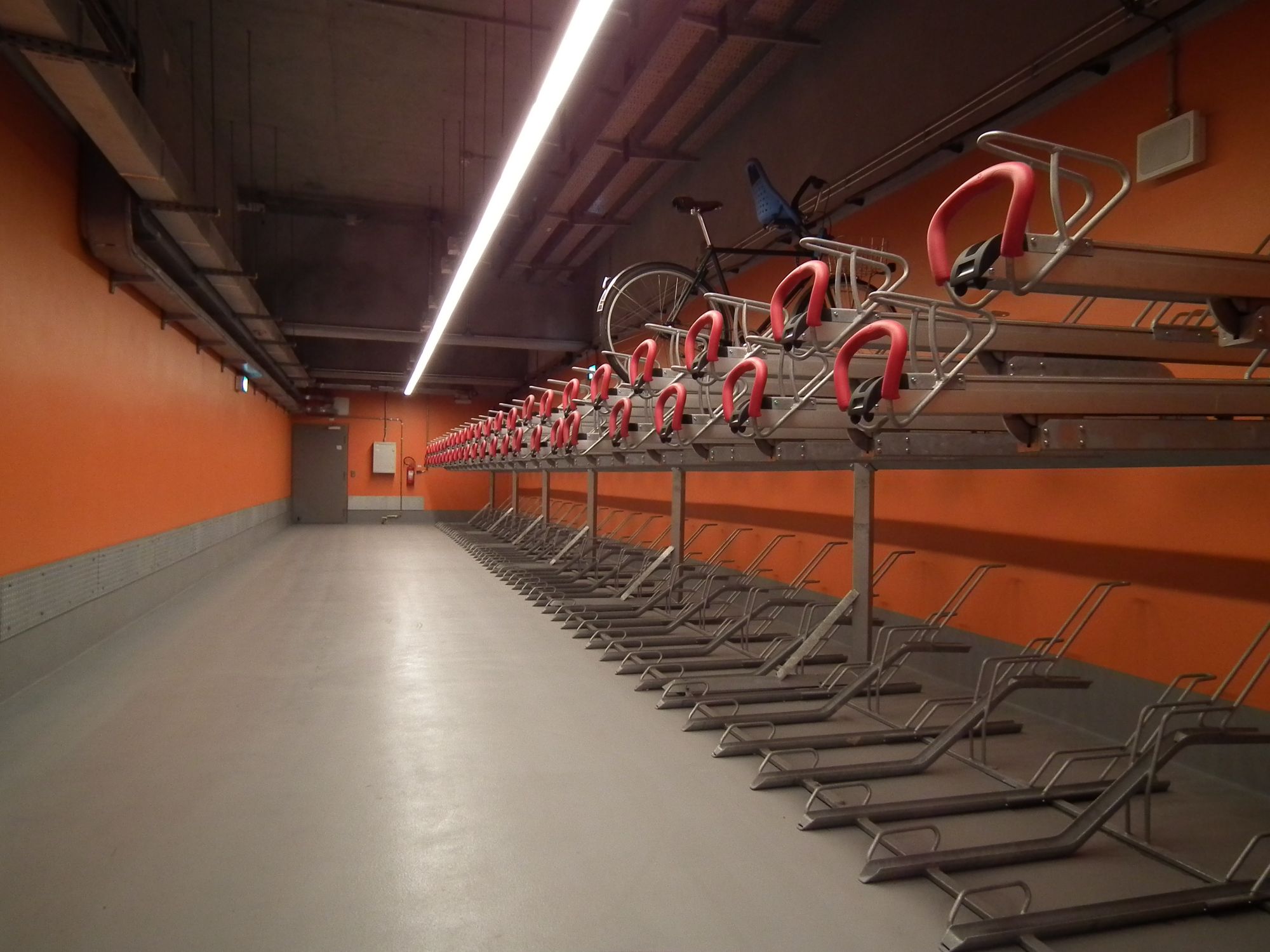 The bike area. A plain concrete space, with a long bike rack (wild guess: space for 120 bikes?) along one wall. The two long side walls are orange, as are the grips on the bike racks.