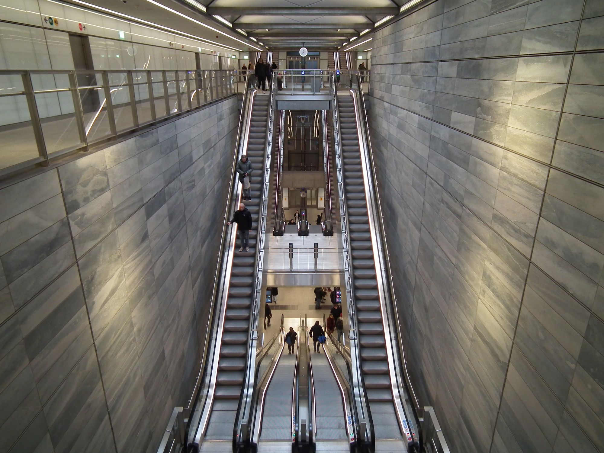 Inside the main station well. We can see the various escalators, nicely symmetrically arranged, and we can see right down to the platform level. The two side walls are tiled in a marble-effect grey.