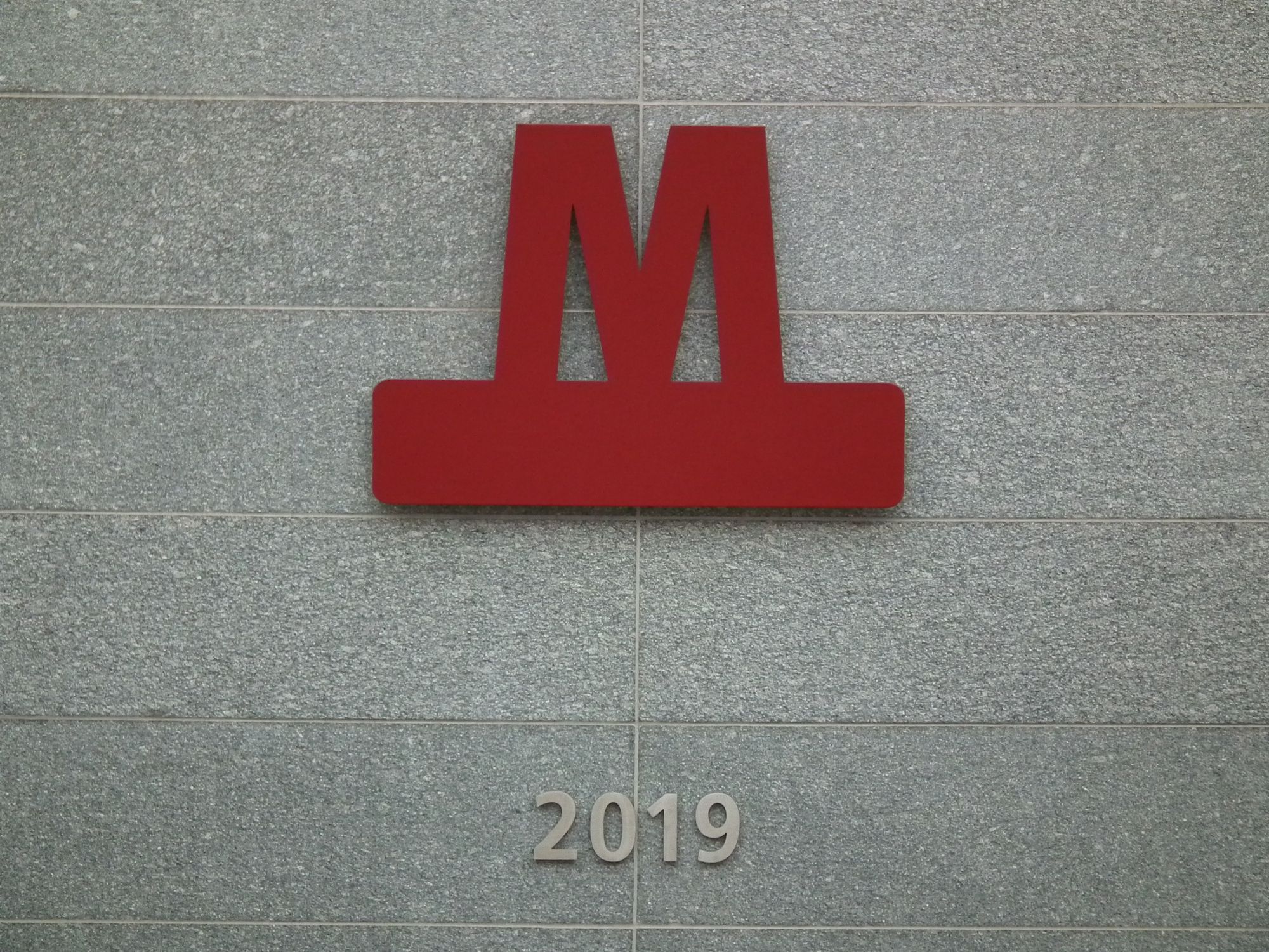 On a speckled grey tiled background, the metro logo (which is a red 'M' on top of a thick red rectangle), and '2019' in silvery metallic figures.