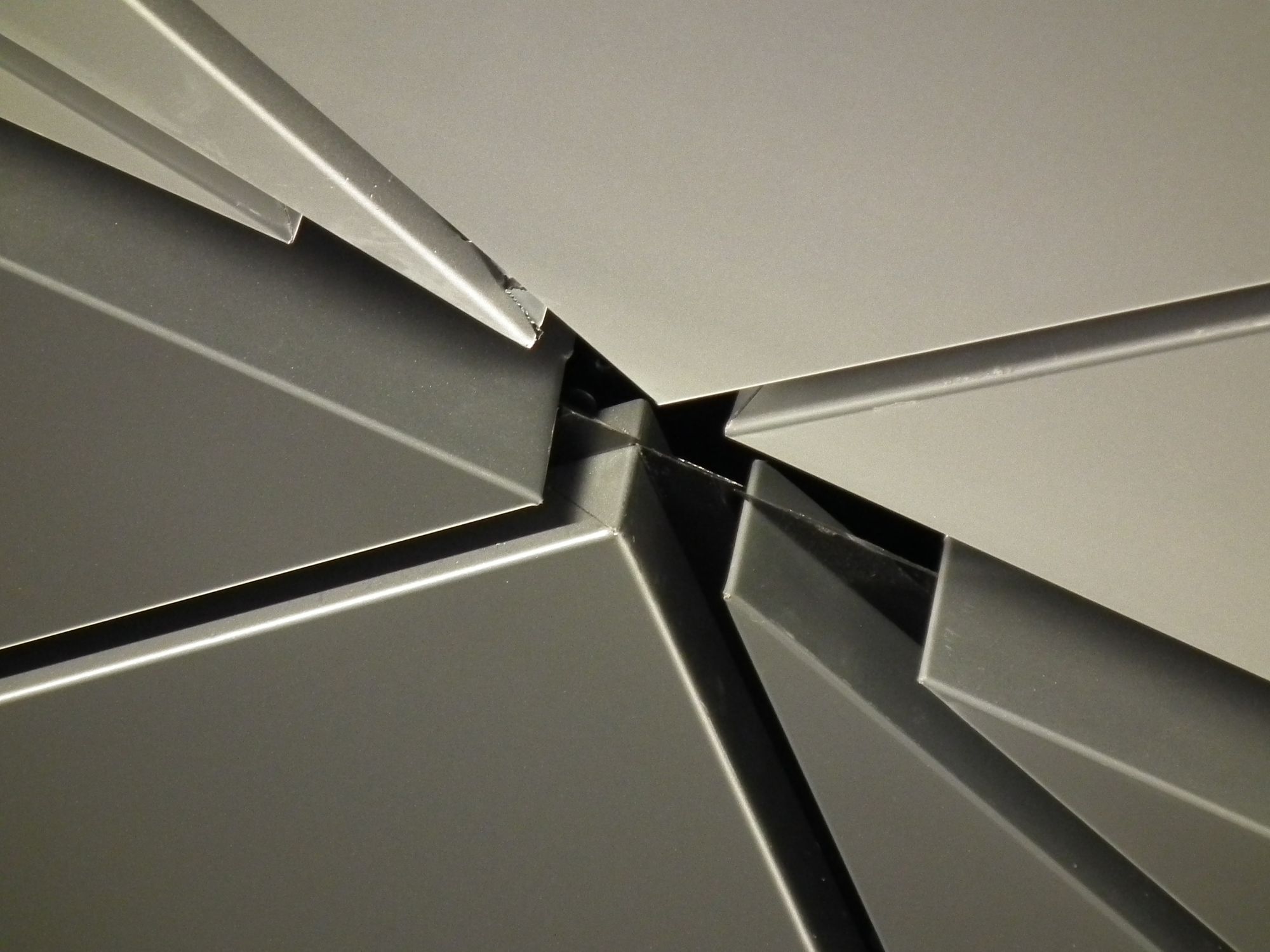 Close-up of part of the roof, where 8 triangular metallic panels meet. Its asymmetrical: some of the points are very acute, some less so. One is almost a right angle. One looks like it might be obtuse.