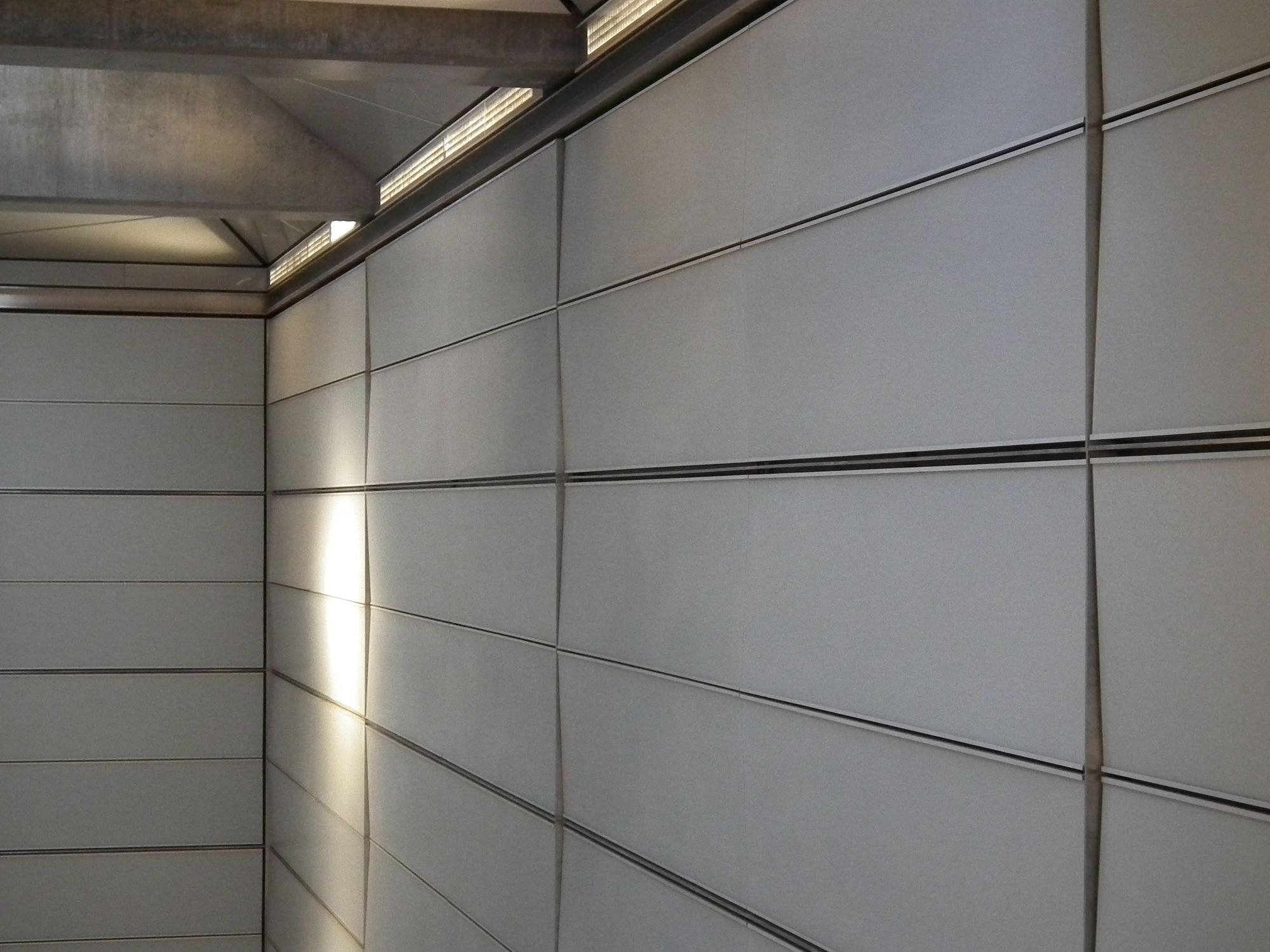 An angled view of the side wall, with plain grey rectangular panels. However, some or all of the panels are not mounted flat to the wall, giving a kind of gentle wave effect.