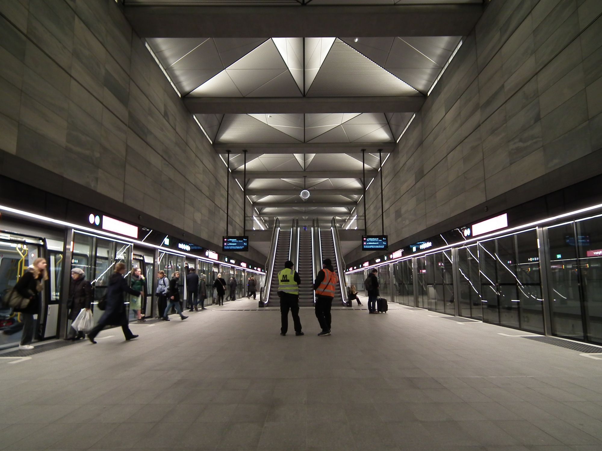 Similar to the above picture, but the reverse angle. More people, boarding and alighting the train; a whole row of the skylights; three escalators connecting this area to the ticket hall above.