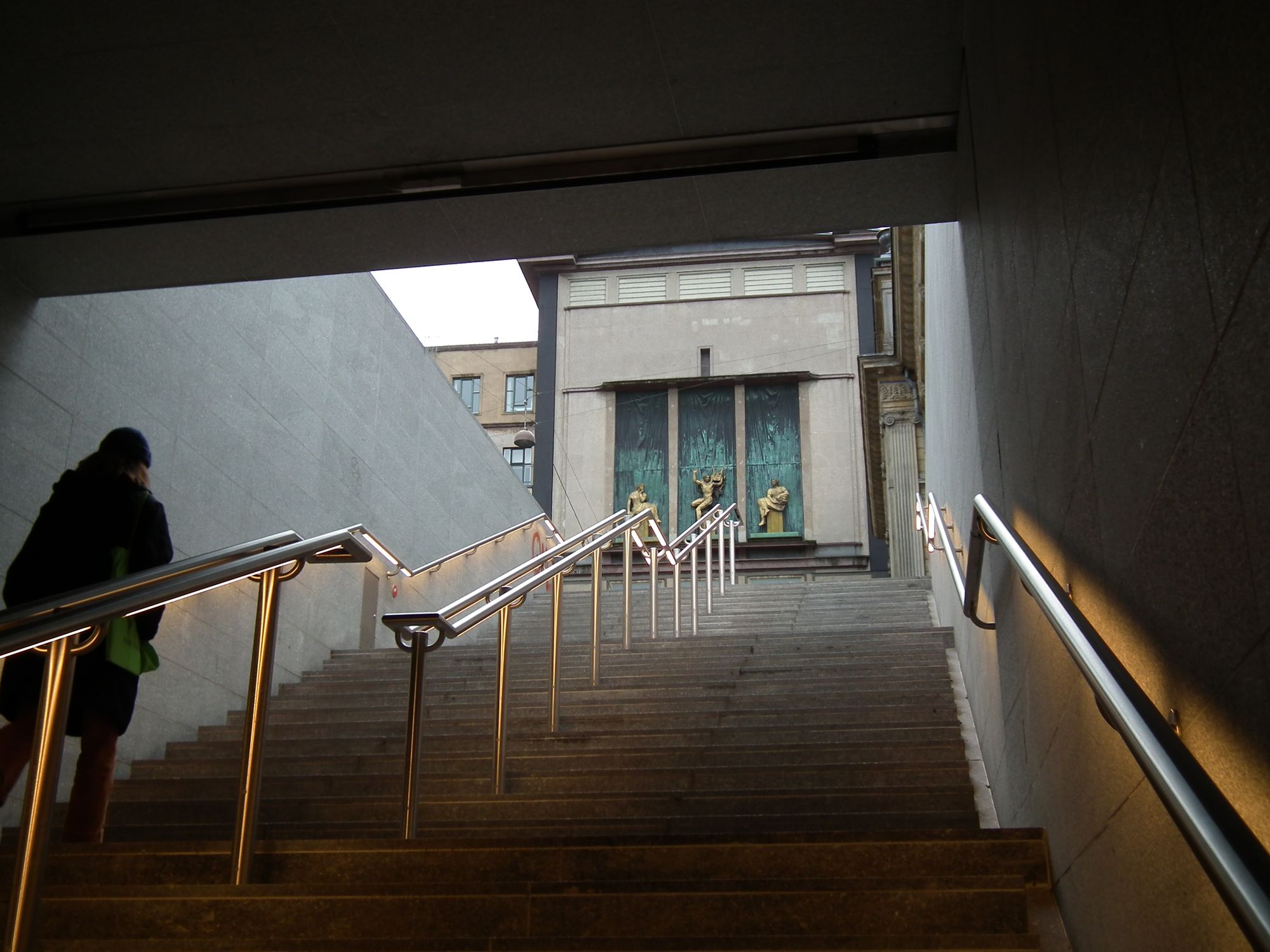 Steps up to street level. At the top of the steps we see the decorated theatre, here with a triptych of three golden relief-statues.