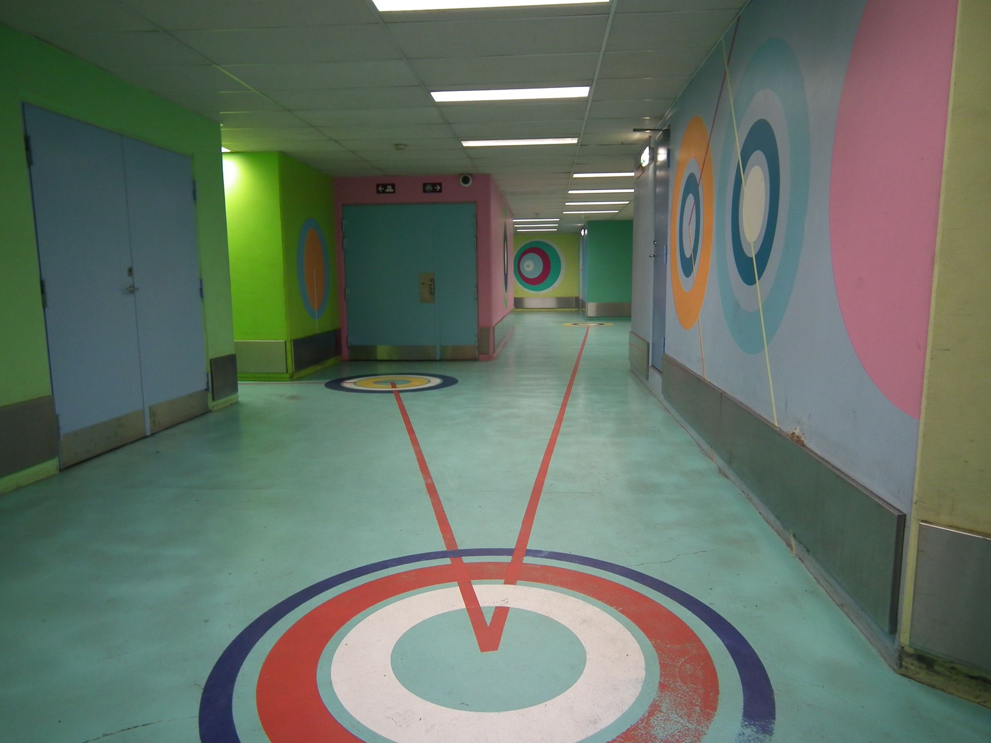 The corridors around the back / bike area of Kongens Nytorv station. The floor and walls are all painted in bright colours. There is a theme of concentric / nested circles, sometimes connected to each other with thick, bright, straight lines.