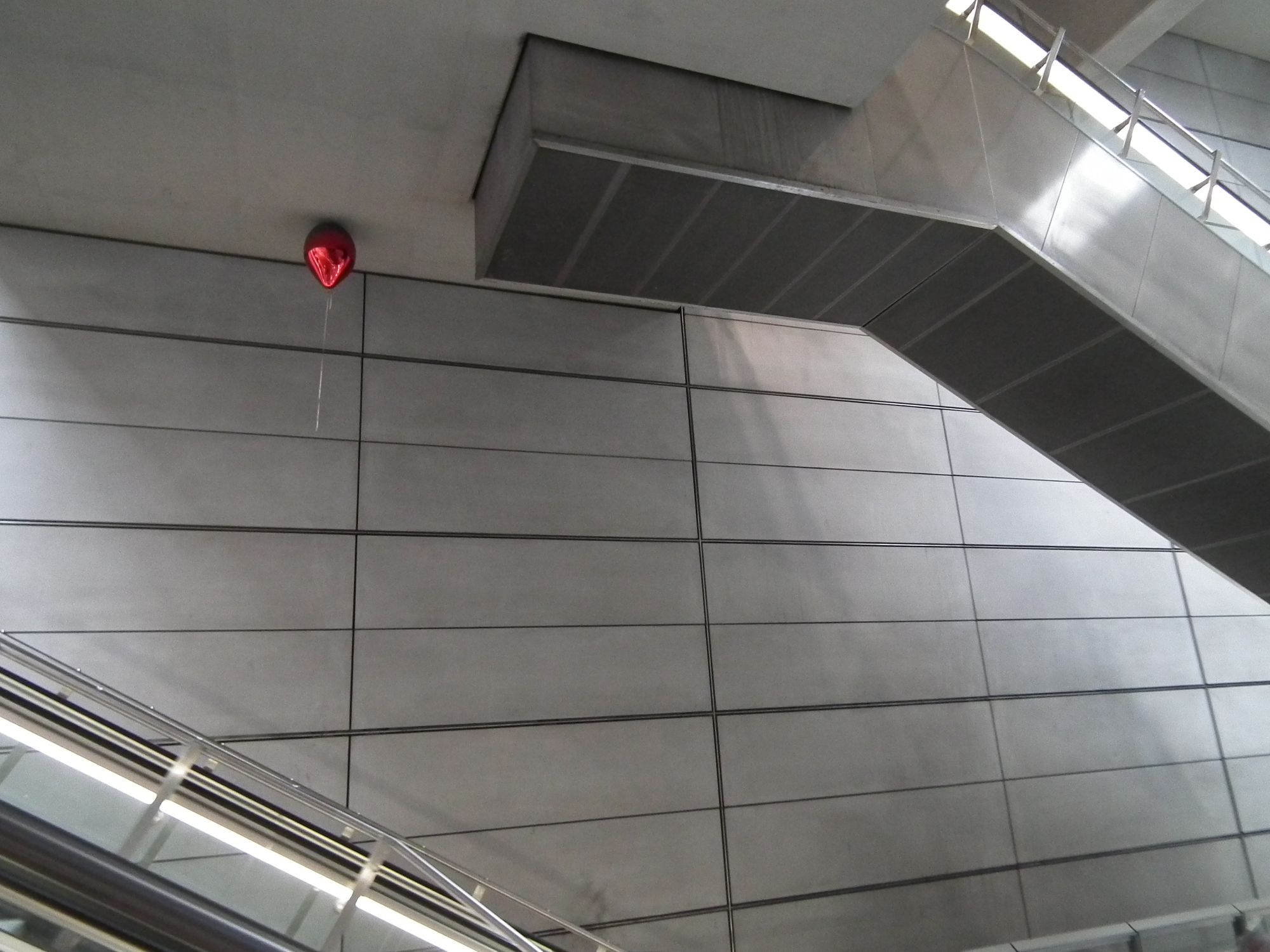 Grey wall, grey escalators, grey ceiling. But up against the ceiling: a shiny red metallic balloon.