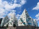 A new mixed residential / commercial building, on former dock land. It is composed of several towering parts, about 10 storeys tall; they are white, with an ice-blue glass surrounding each balcony. The roofs are steep and spikey, and most of the windows are either right-angled triangles, or contain a triangular pane.