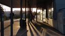 People waiting on a train station platform. The sun is directly in front of us, and quite low, but we can't directly see it. What we do see is the long shadows cast by people, pillars, and other objects on the platform.
