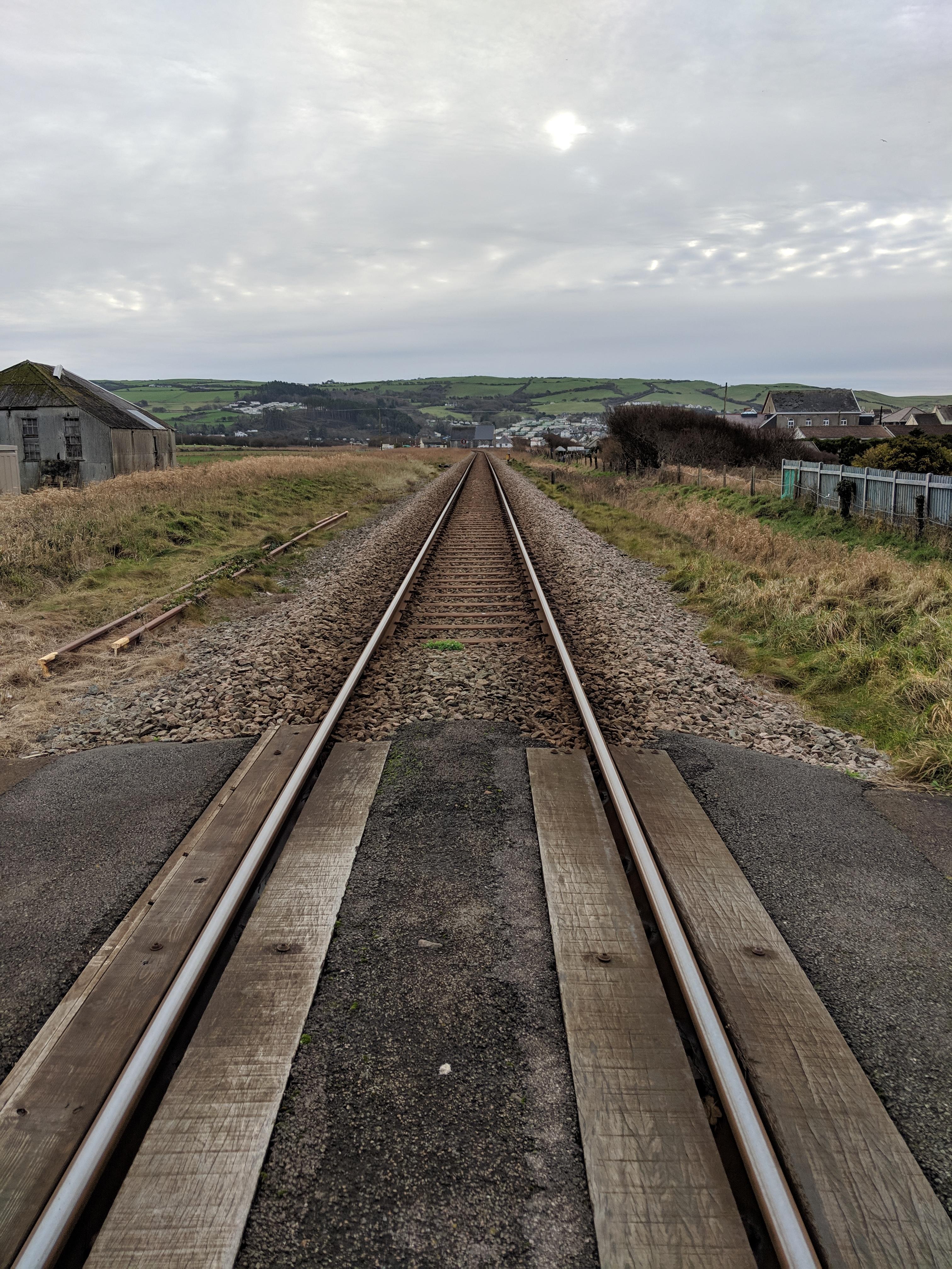A single track of railway, stretching in a very straight and level line, directly away from the camera. We are stood on an unprotected level crossing. It's a grey, cloudy December day on the west coast of Wales.